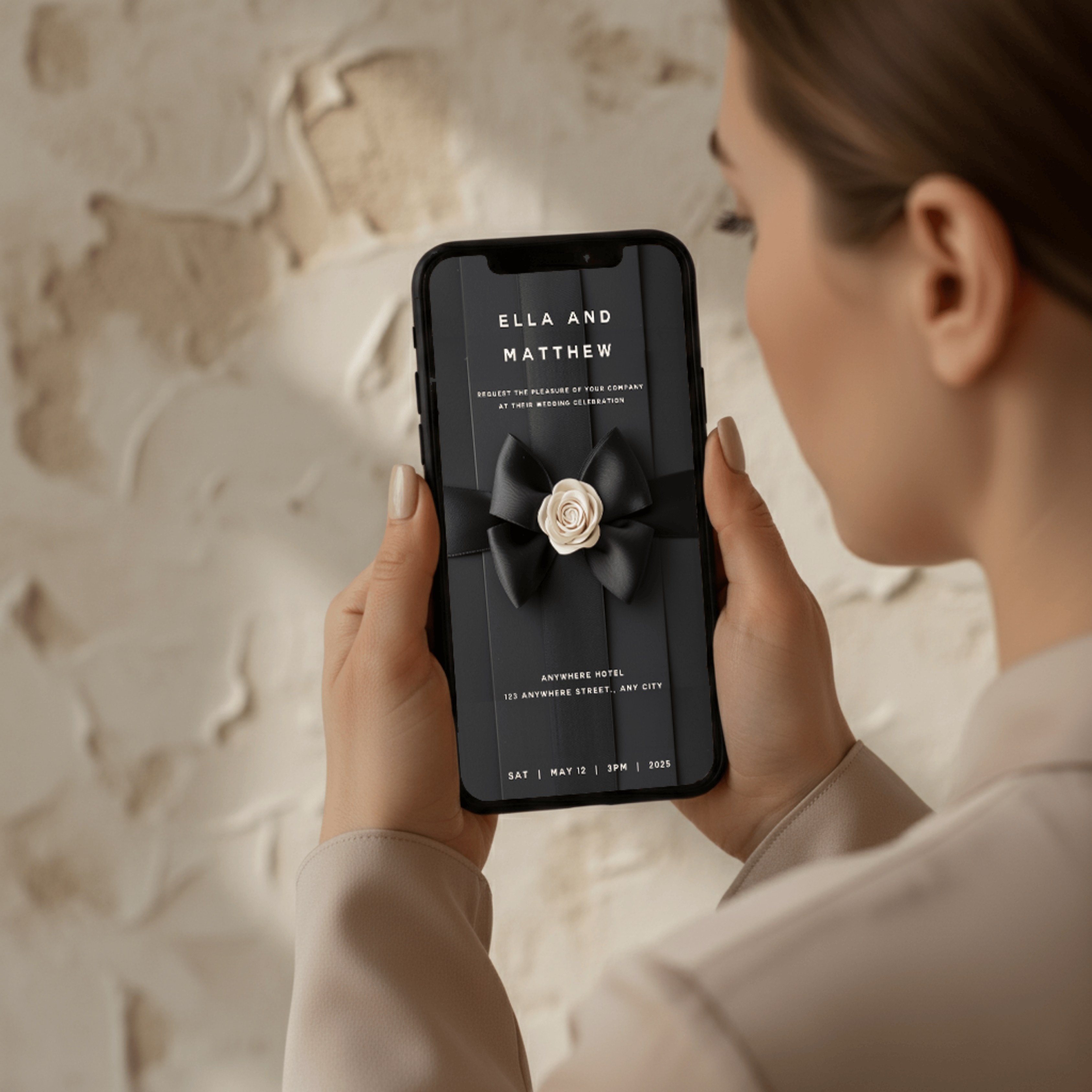 Woman holding digital Chanel-inspired wedding invitation with black satin bow and camellia flower — editable Canva template for modern luxury weddings.