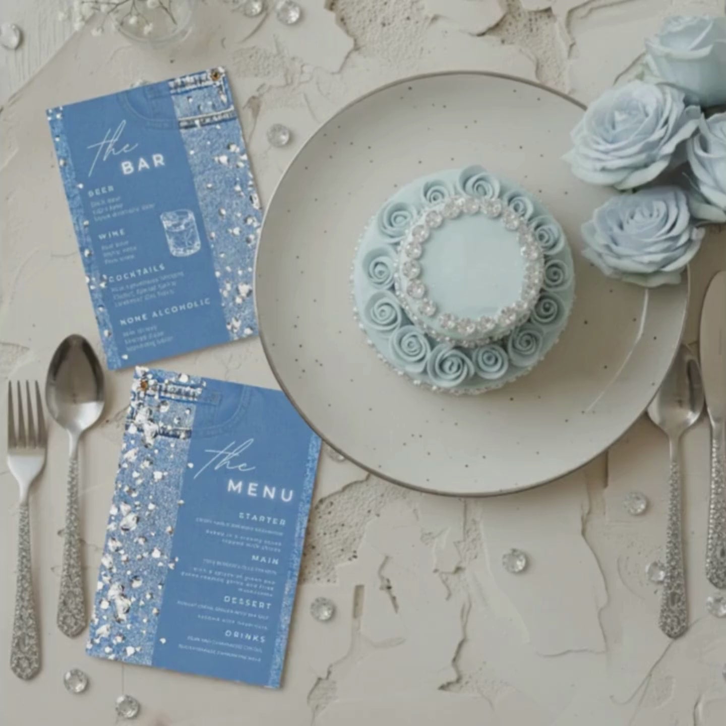 Denim and Diamonds themed party decor  editable Canva menu and bar cards displayed beside a pearl-decorated blue cake with silver cutlery and roses luxury birthday table setup aesthetic.